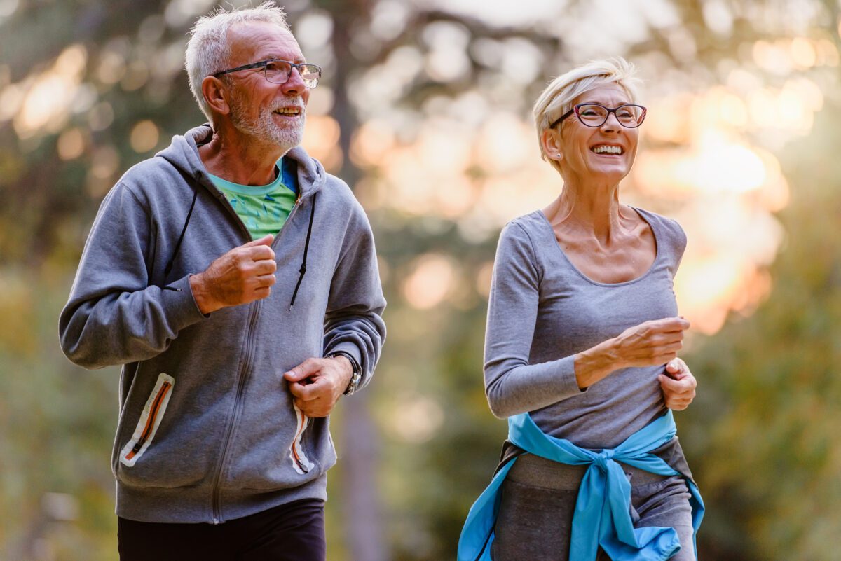 Cheerful active senior couple jogging in the park. Exercise together to stop aging.