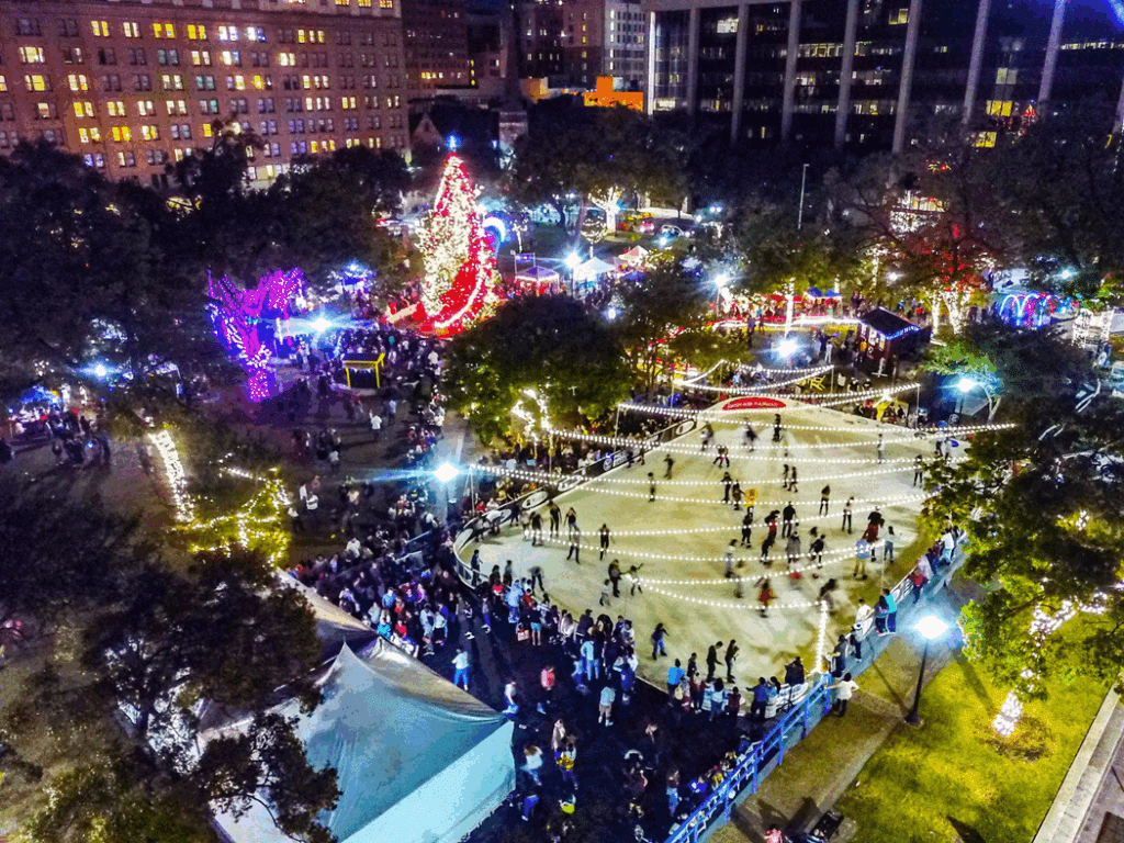 Aerial view of Travis Park in downtown San Antonio featuring a holiday ice-skating rink surrounded by colorful lights and festive crowds. Photo credit: visitsanantonio.com