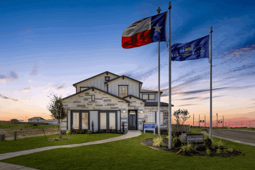 Modern stone and siding model home with Texas and American flags at sunset in a new Hakes Brothers San Antonio community.