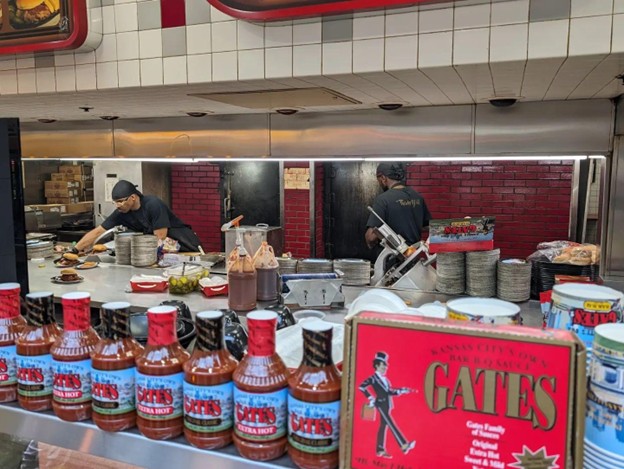Chefs making food in the Gates Bar-B-Q kitchen with jars of barbeque sauce in the foreground