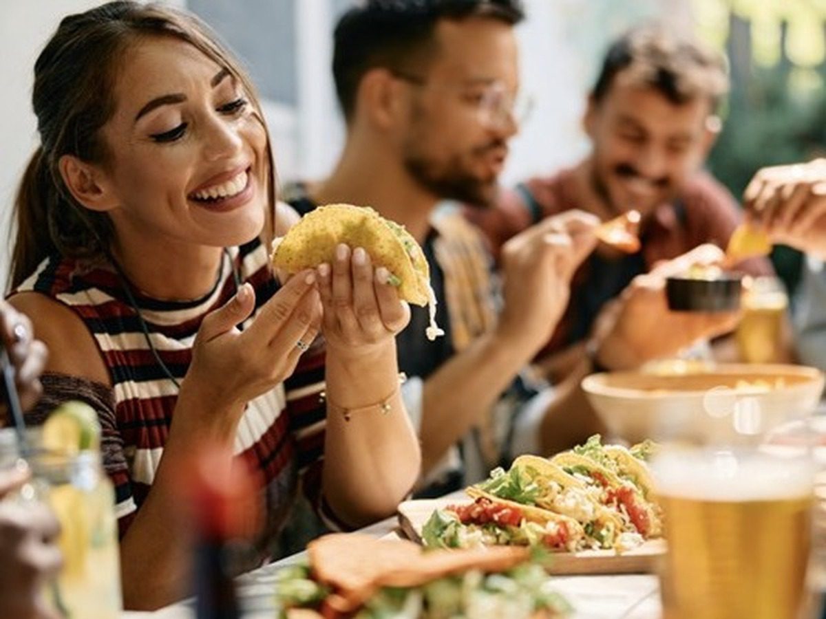 Happy woman eating tacos during lunch with friends in Mexican restaurant
