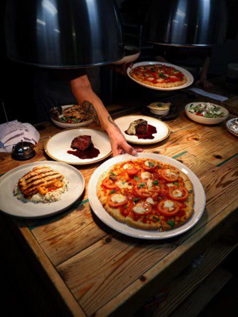 Many plates of food served by a chef onto a wood table