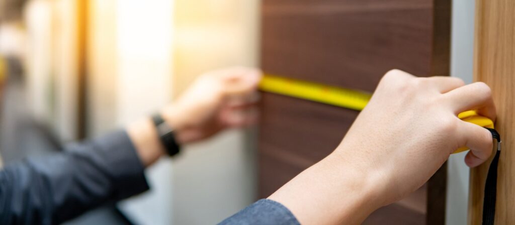 Man using tape measure on cabinet panel choosing materials for built-in furniture design.