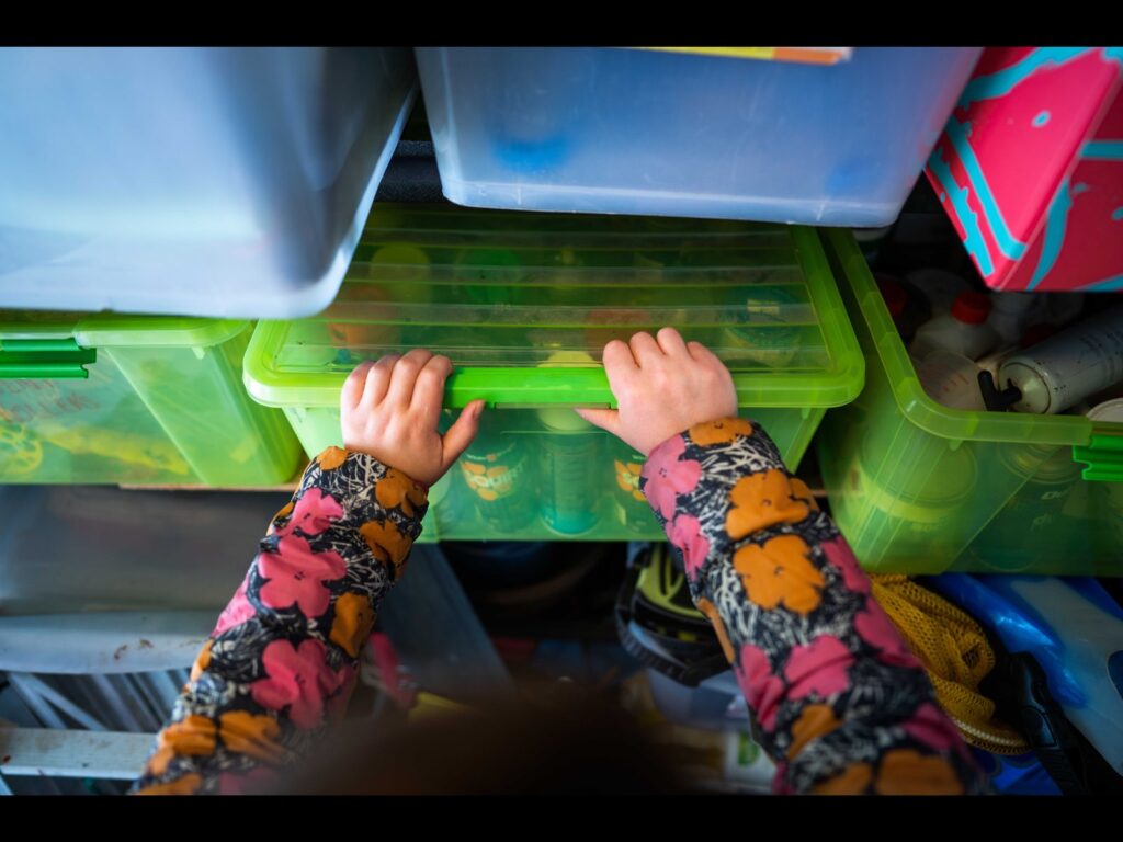 Girl putting away a full plastic bin on a shelving unit of full plastic bins