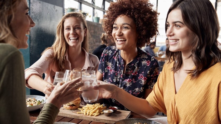 Four Young Female Friends Meeting For Drinks And Food Making A Toast In Restaurant