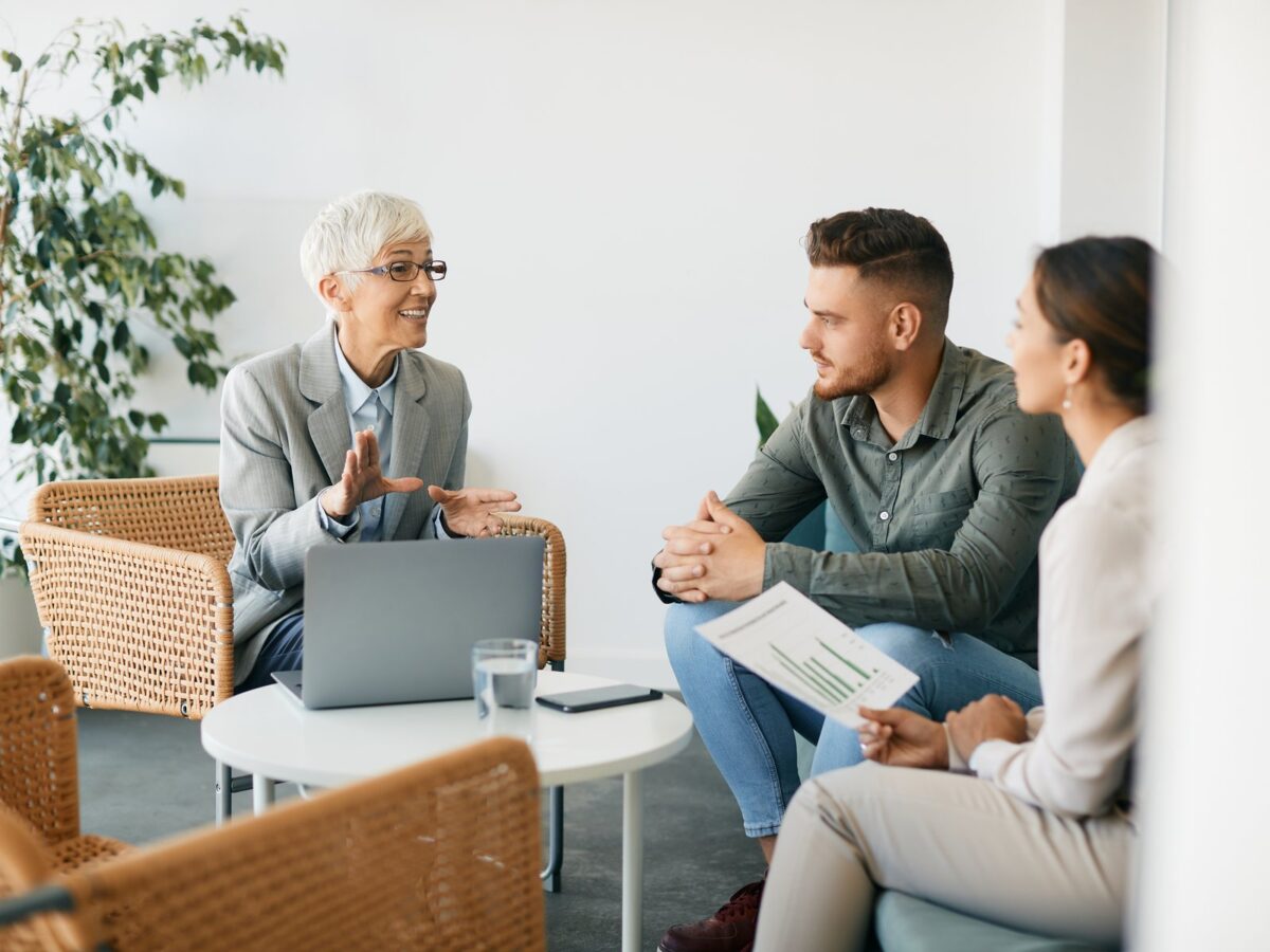 Happy real estate adviser talks to couple during the meeting in office.
