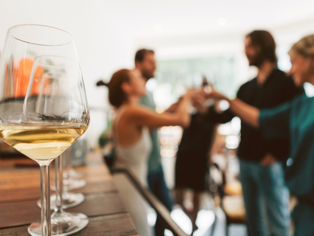 Filled wine glasses on table with group of friends in background toasting wine glasses together.