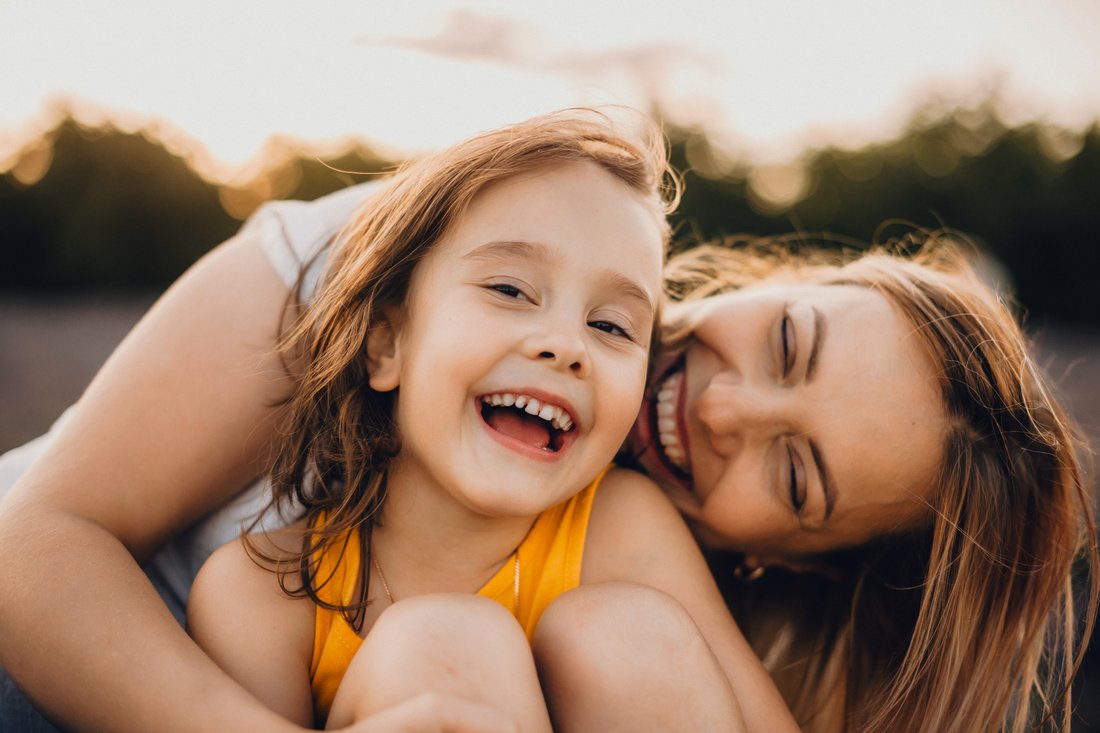 Mom and daughter smiling together outside at sunset
