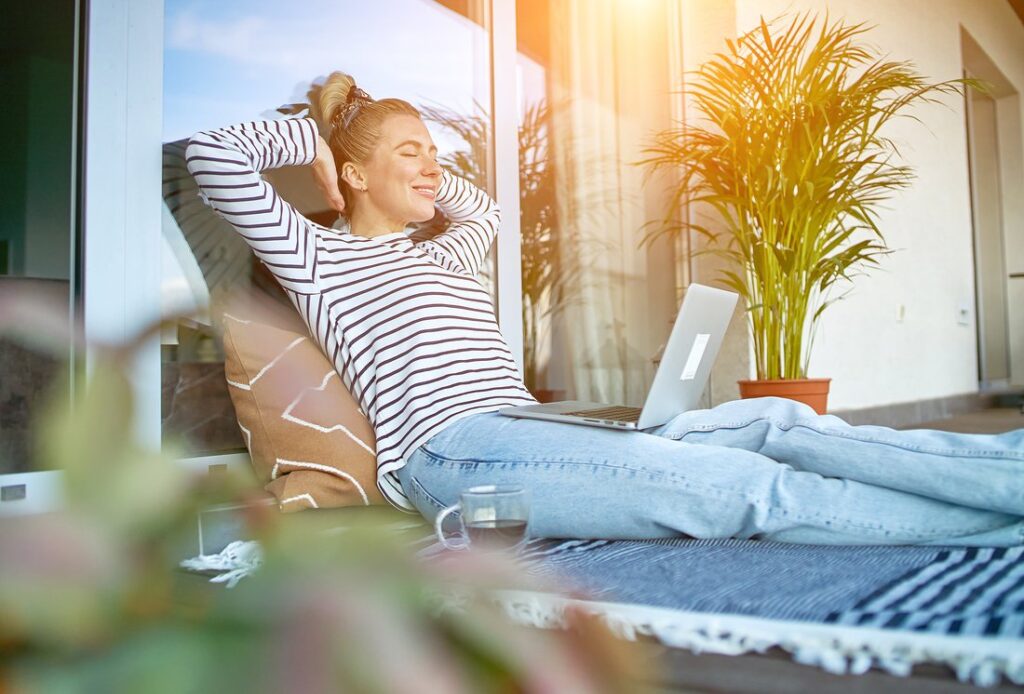 Woman working on her laptop on her back patio with a cup of coffee