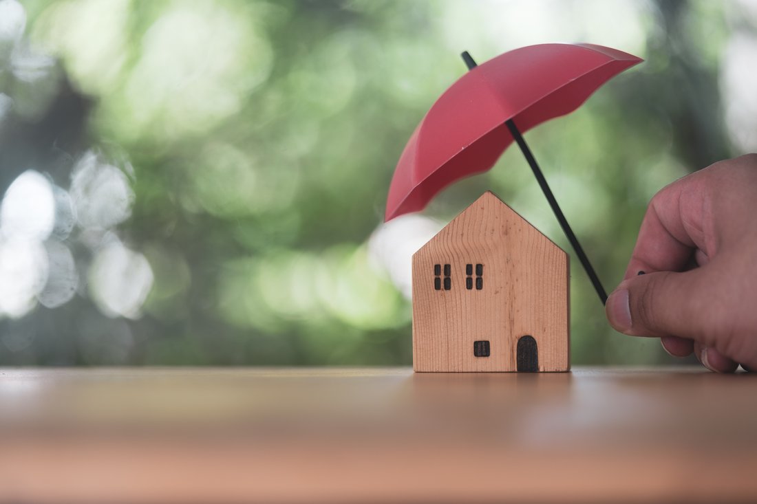 Person holding small red umbrella over a miniature home