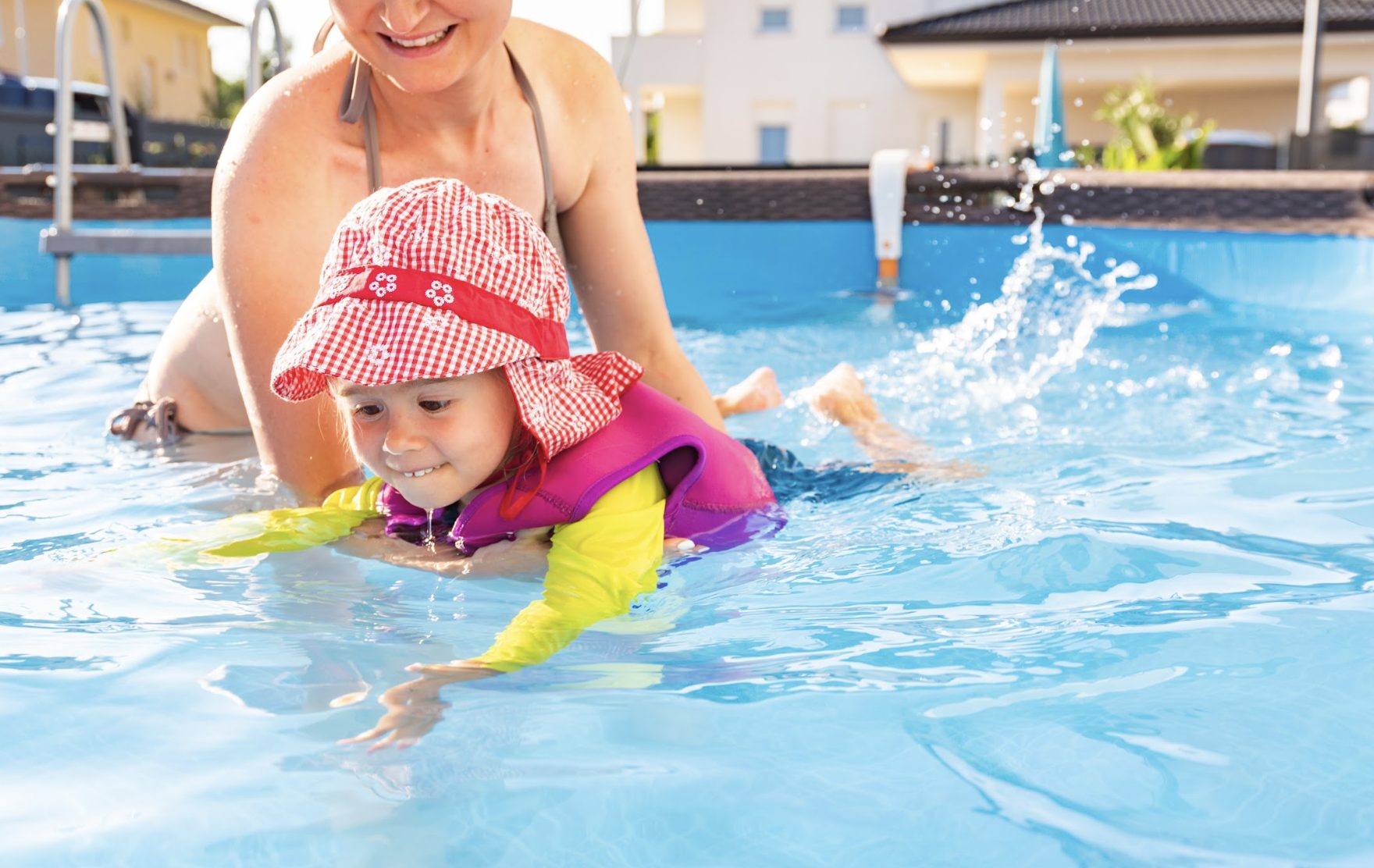 Mother teaching young child to swim in a backyard pool