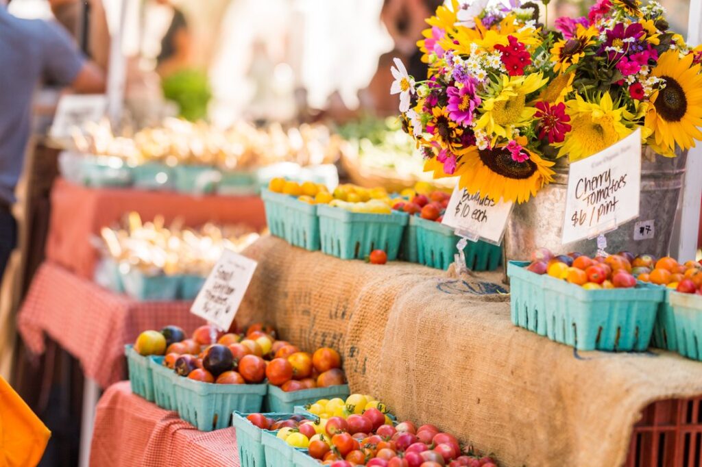 Farmers market stand with fresh produce and flowers.