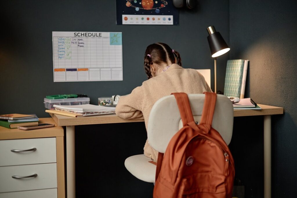 Girl sitting at desk studying with books and notebooks and a calendar on the wall.