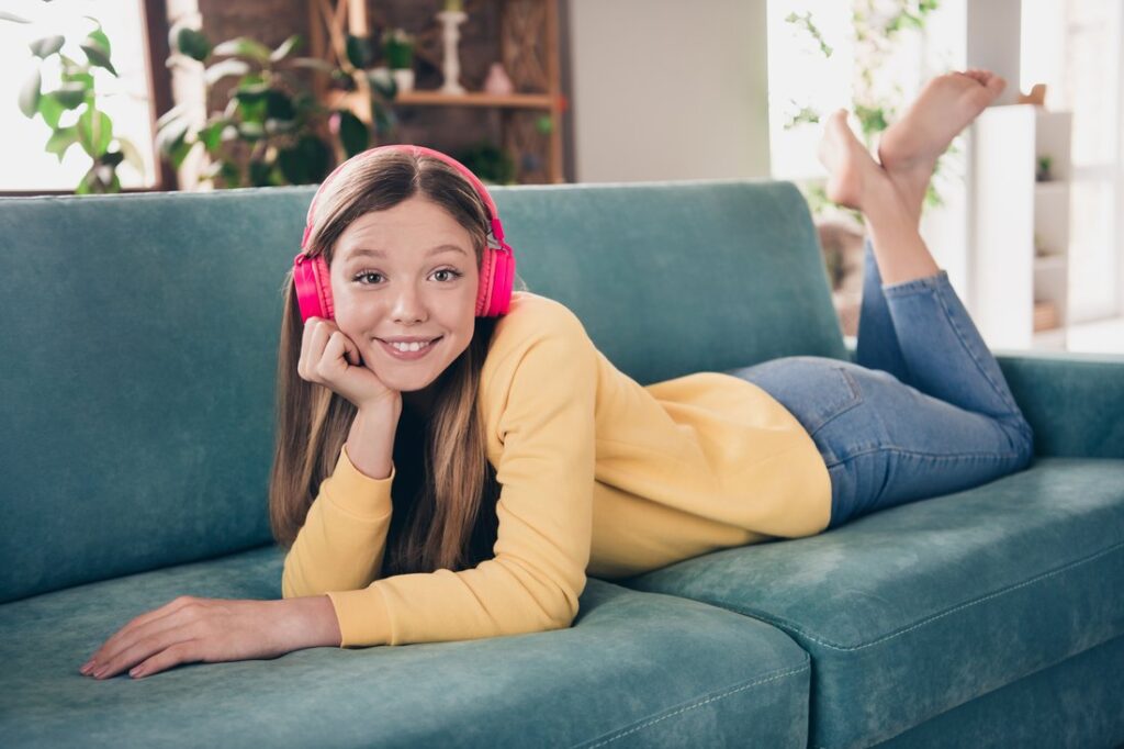 Teen girl laying on the couch listening to music on headphones.