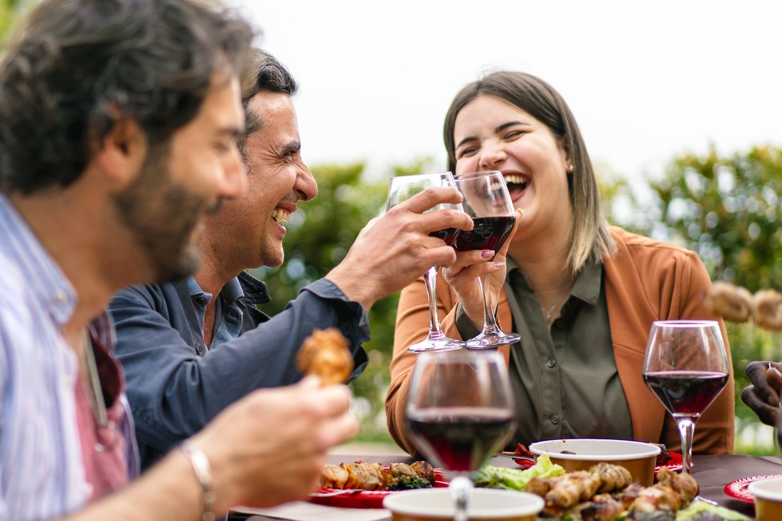 Happy group of friends toasting with red wine at an outdoor dinner.