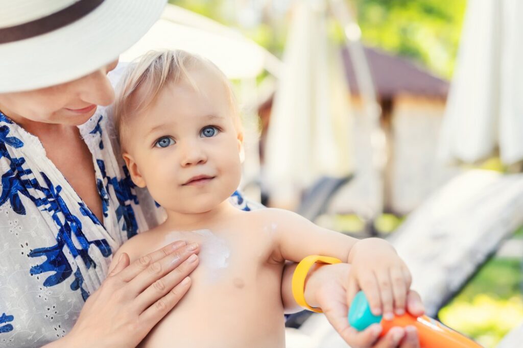 Mother applying sunscreen protection on toddler boy.