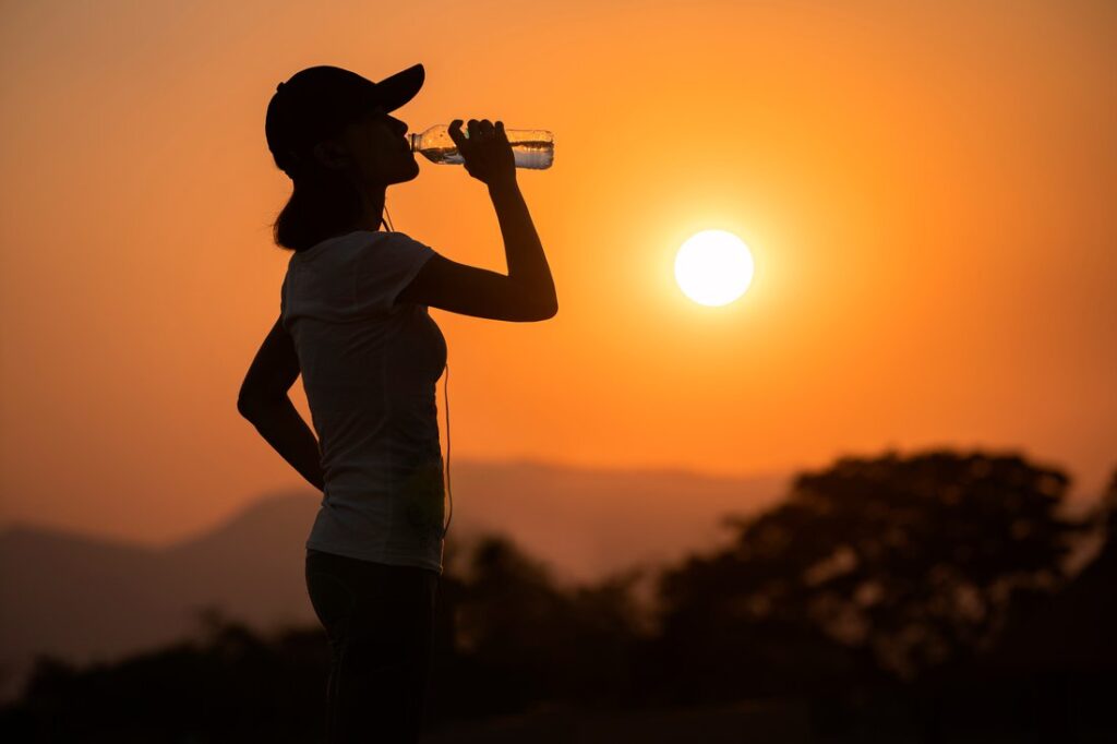 Woman drinking water bottle after workout in the summer heat.