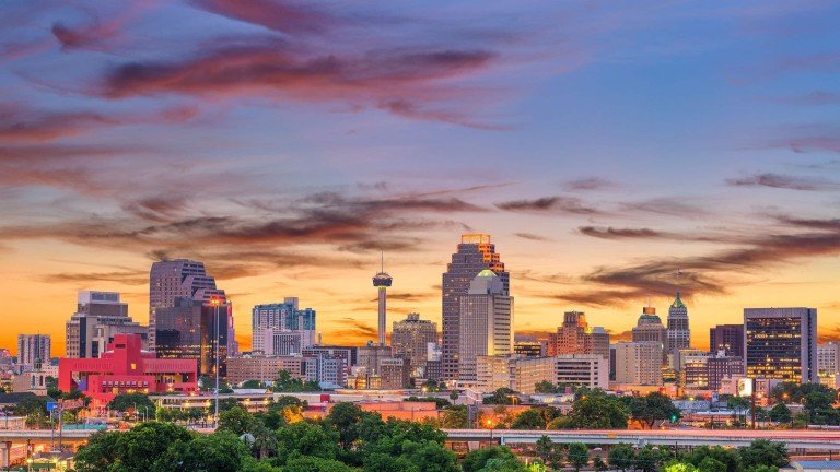 Downtown San Antonio skyline at sunset showcasing the Tower of the Americas, modern buildings, and colorful evening sky.