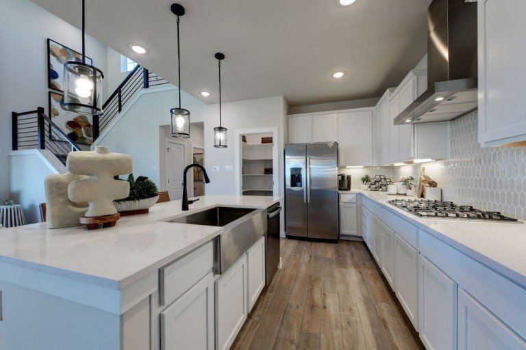 Modern gourmet kitchen in a new construction home at La Cima in San Marcos, TX featuring white cabinetry, large island, and open-concept design.