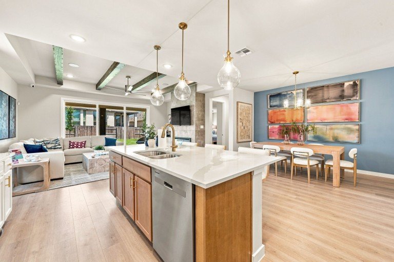Modern open-concept kitchen with quartz island, pendant lighting, and spacious living area in a new construction home at La Cima in San Marcos, Texas.
